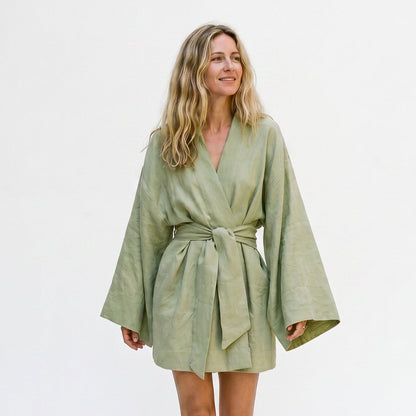 Green Dress - Model wearing a relaxed linen-textured long-sleeve mini wrap dress with wide sleeves and a self-tie waist belt.