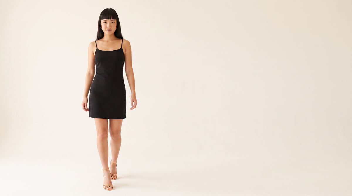 Woman in a short black slip dress walking in gold metallic strappy stiletto heels