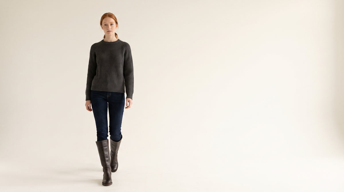 Woman in a charcoal knit and dark jeans walking in dark brown block heel knee high boots